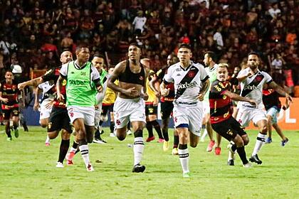 Jogadores de vasco e sport recife corendo em campo, em meio a invasão de torcida na ilha do retiro