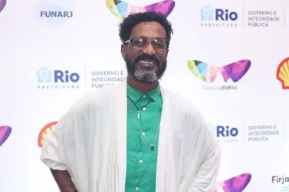 Luis Miranda de manta branco, camisa social verde, de oculos de grau, sorrindo, com as mãos na cintura durante passagem pelo Festival do Rio