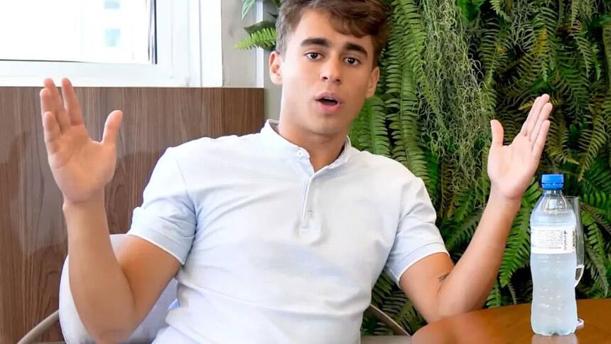 Nikolas Ferreira de camisa branca com os braços abertos, sentado durante entrevista