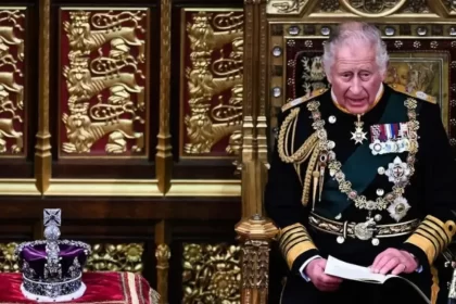 Rei Charles III sentado no trono, ao lado da coroa