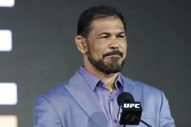 Rodrigo Minotauro de camisa social azul, usando barba e bigode, com semblante sério em apresentação do UFC