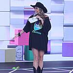 Adriane Galisteu de chapéu de Cowgirl preto, segurando fichas e microfone durante apresentação do Teleton