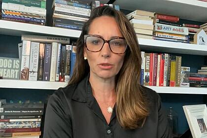 Ana Paula Henkel em trecho de um vídeo, com uma enorme estante de livros ao fundo