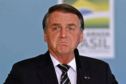 Bolsonaro de paletó preto e gravada listrada fazendo biquinho de choro durante coletiva no Ministério da Saúde