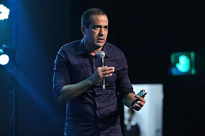 Bruno Reis de camisa social preta, segurando um microfone durante coletiva do Festival Virada Salvador