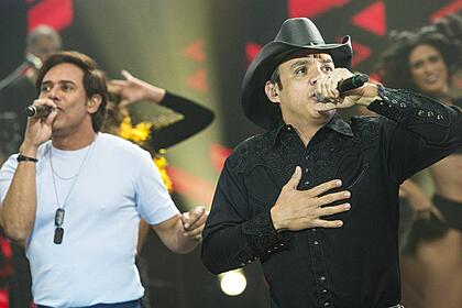 Guilherme de camisa básica branca, Santiagod e camisa social preta e chapéu de cowboy durante performance no Faustão na Band