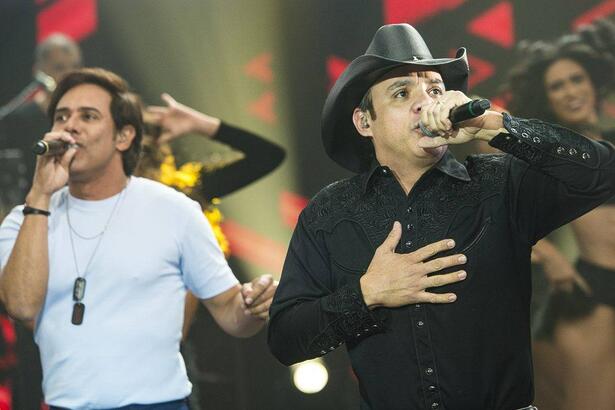 Guilherme de camisa básica branca, Santiagod e camisa social preta e chapéu de cowboy durante performance no Faustão na Band