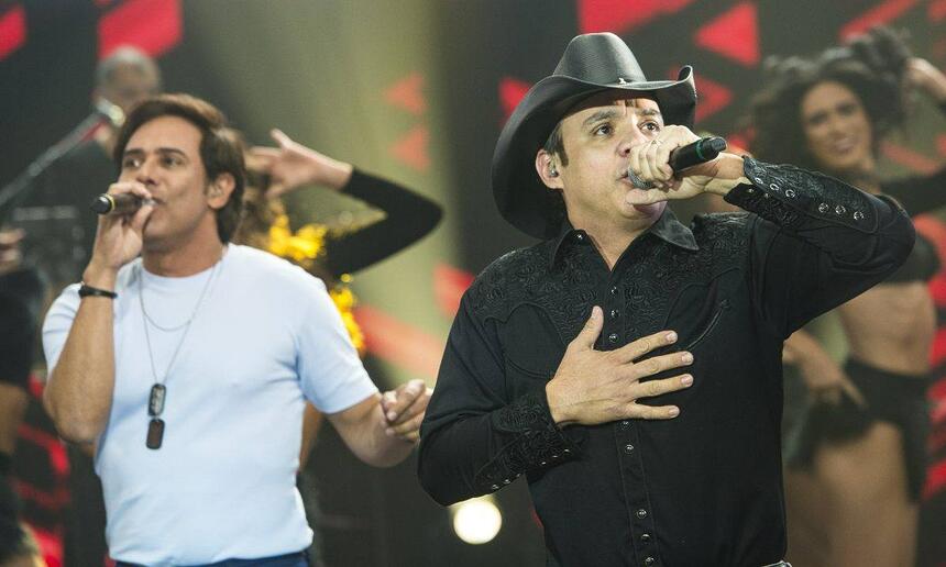 Guilherme de camisa básica branca, Santiagod e camisa social preta e chapéu de cowboy durante performance no Faustão na Band
