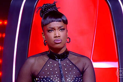 Iza, com uma roupa de renda preta, sentada na cadeira de técnica, com cara de assustada, em trecho do the voice brasil 11