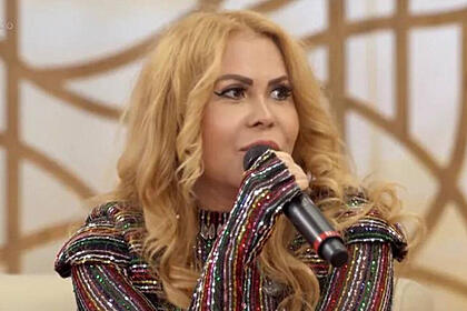 Joelma, com um microfone nas mãos, sentada no sofá do Encontro, com uma roupa brilhosa