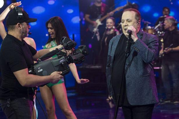 José Augusto de blazer e camisa preta, segurando o microfone durante performance no Faustão na Band
