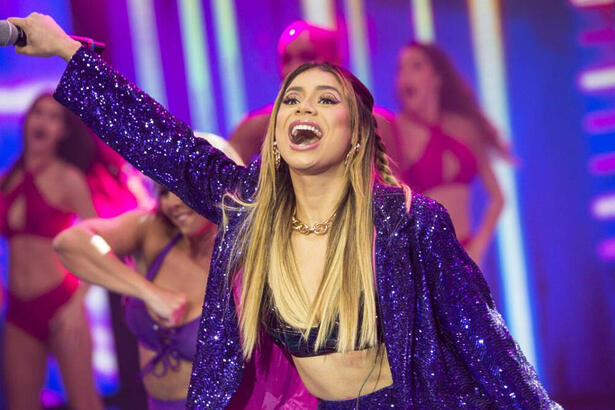 Lexa com o braço pra frente, sorrindo, com a boca aberta, durante gravação do Faustão na Band