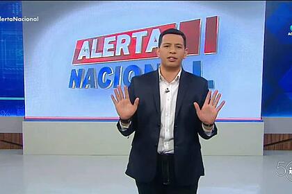 Luiz rodrigues mostrando as palmas das mãos, nos estúdios do alerta nacional, em frente ao telão