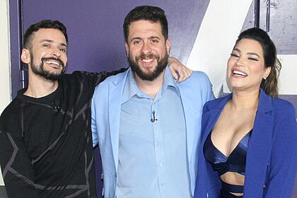 Fefito de camisa preta sorrindo, ao lado de Mauricio Meirelles, de blazer, camisa social e calça de linho azul claro, ao lado de Raissa Barbosa, sorrindo, de blazer azul e top preto durante gravação do Foi Mau, da RedeTV!