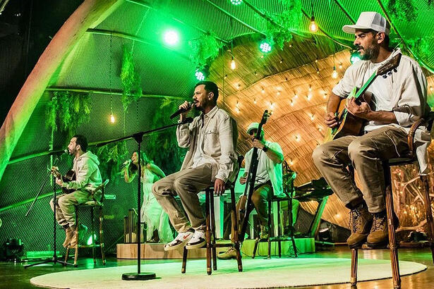Integrantes da Planta e Raiz sentados, de camisa branca e calça marrom durante gravação do 'Acustico Planta e Raiz'