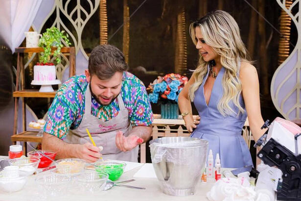 Camilo ao lado de Beca Milano, em frente a sua bancada, em trecho do episódio final do Bake Off Brasil