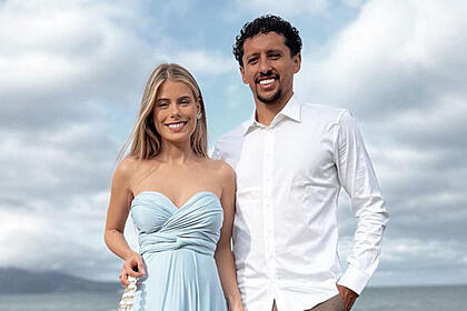 Carol Cabrino, com um vestido azul, ao lado de Marquinhos, com uma blusa social branca, em foto posada