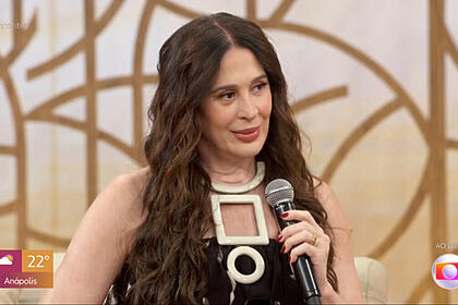 Claudia Raia com um roupa preta e cabelos jogados sobre o ombro, em trecho de sua participação no Encontro, sentada no sofá