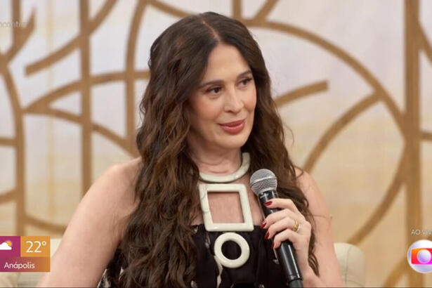 Claudia Raia com um roupa preta e cabelos jogados sobre o ombro, em trecho de sua participação no Encontro, sentada no sofá