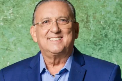 Galvão Bueno de blazer azul e camisa social branca, de óculos de grau, sorrindo durante sessão de fotos da TV Globo