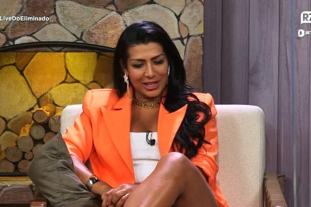 Moranguinho sentada durante Live do Eliminado. Vestida com uma roupa laranja