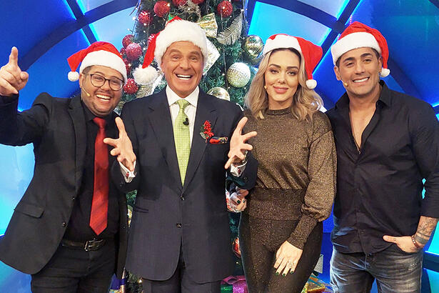 Tânia Mara de camisa e calça em tons de marrom, sorrindo, com gorro de papai noel ao lado de Marcello de Carvalho e a dupla Hugo e Tiago que estão de camisa e calça preta, sorrindo, também com gorro