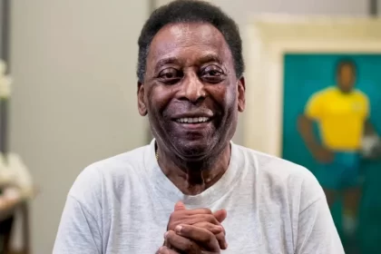 Pelé de camisa cinza, com as mãos juntas, sorrindo durante ensaio fotográfico