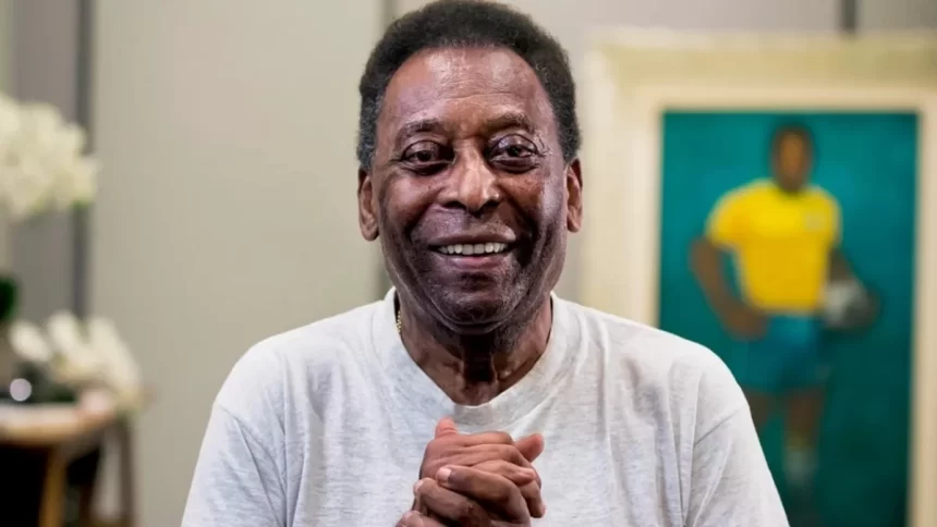 Pelé de camisa cinza, com as mãos juntas, sorrindo durante ensaio fotográfico