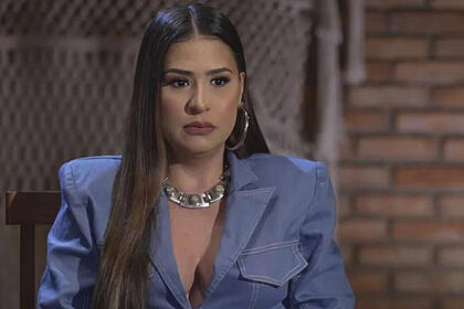 Simone com uma roupa jeans, em trecho da entrevista para o Fantástico, com uma parede ao fundo