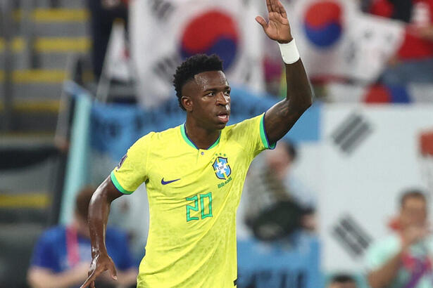 Vinícius Jr, em campo com a camisa do Brasil, com a mão esquerda levantada