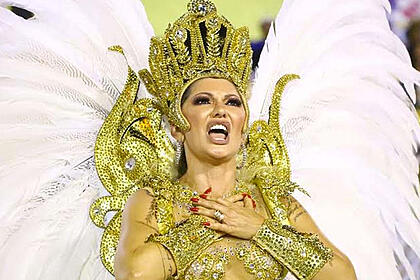 Antonia Fontenelle com as mãos no peito, usando look dourado de carnaval com asas coberta de plumas brancas