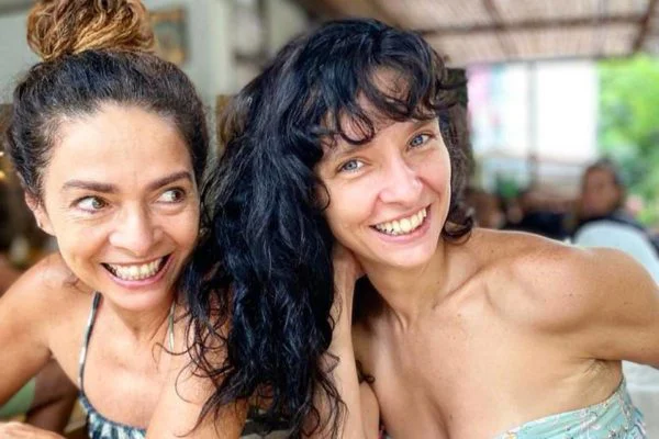 Claudia Ohana de cabelo preso, sorrindo ao lado da filha