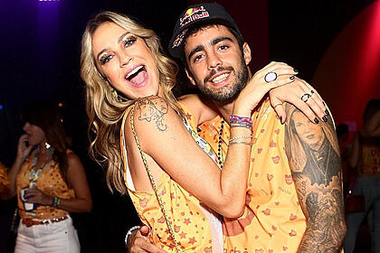 Luana Piovani com a boca aberta, cabelo solto, com as mãos abraças a Pedro Scooby: Pedro Scooby sorrindo, de chapéu preto; ambos usando abadá larankja