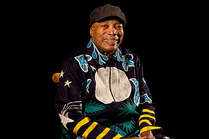 Milton Nascimento sentado, com uma roupa estampada, em trecho do Som Brasil