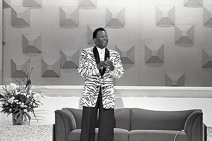 Pelé de pé, vestido com blazer branco e preto e calça preto, em participação no programa da Hebe, no SBT.