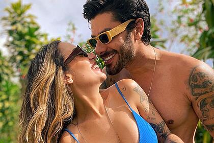 Renan Oliveira com óculos de sol, sorrindo, sem camisa, abraçado com a namorada de biquini azul e óculos de sol