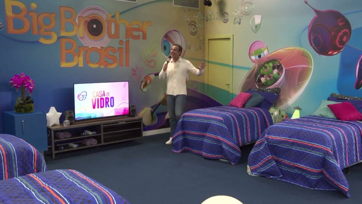 Tadeu Schmidt de camisa branca e calça dentro da Casa de Vidro, apresentando o espaço em chamada