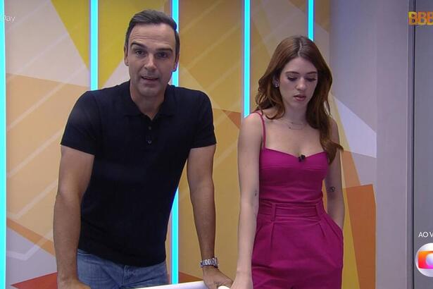 Tadeu Schmidt, de camiseta polo preta e calça jeans, e Ana Clara, com um vestido rosa, direto da casa do BBB 23, durante trecho da divulgação dos nomes ao vivo