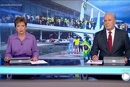 Âncoras do Joral da Record sentados no estúdio da Record TV apresentando telejornal