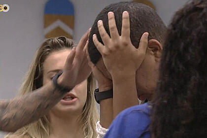 Bruno Gaga com a mão na cabeça, em pé, sendo acolhido por brothers na cozinha do BBB 23