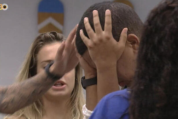 Bruno Gaga com a mão na cabeça, em pé, sendo acolhido por brothers na cozinha do BBB 23