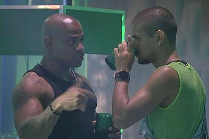 Cezar segurando um copo de frente para Gabriel que está com um copo na boca.