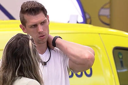 Cristian com a mão no pescoço, de camisa branca, ao lado de Amanda, que também está de camisa branca, de costa