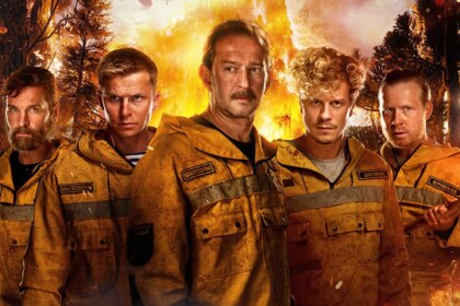 Homens com fardas de bombeiros sujos em meio a uma mata pegando fogo em cena do filme Heróis de Fogo