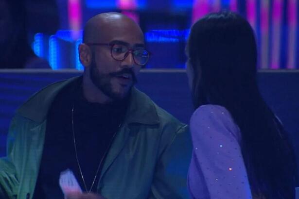 Ricardo com semblante sério de frente para Larissa que aparece de costas na imagem.