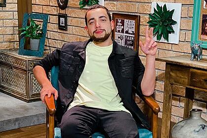Lucas Selfie sentado com camisa amarela clara, jaqueta jeans preta, fazendo um 2 com a mão esquerda, com semblante sério nos estúdios de A Fazenda, da Record TV