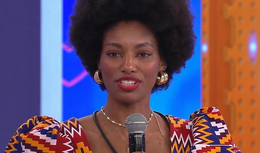 Tina com camisa personalizada em tribal nas cores amarela, vermelho, azul e branco, segurando o microfone