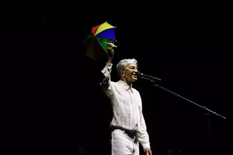 Caetano Veloso de camisa e calça branca suspendendo uma sobrinha de frevo durante show em recife