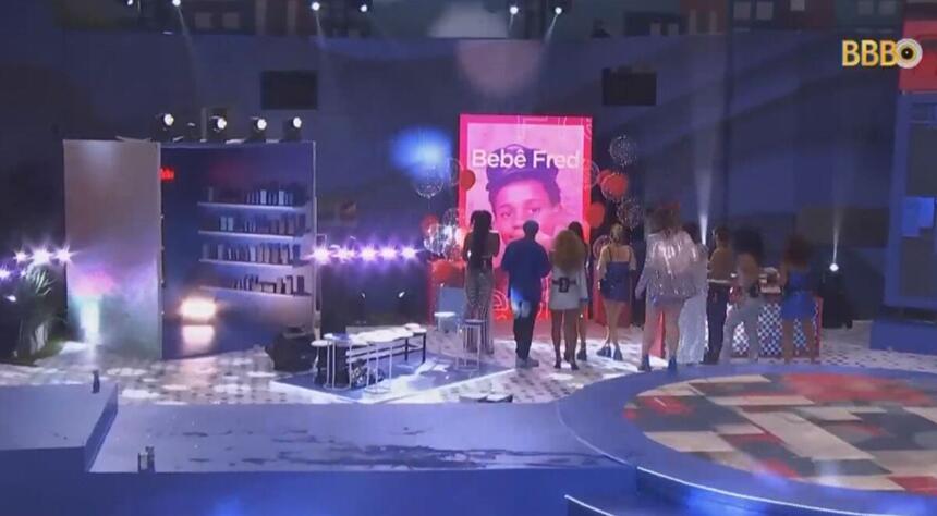 Participantes em pé na festa do BBB 23 de frente para o telão que aparece Fred Nicácio criança