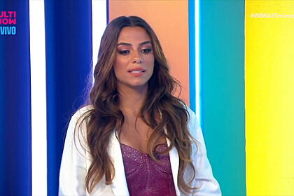 Key Alves de blazer branco, camiisa roxa, em pé durante gravação de programa de TV